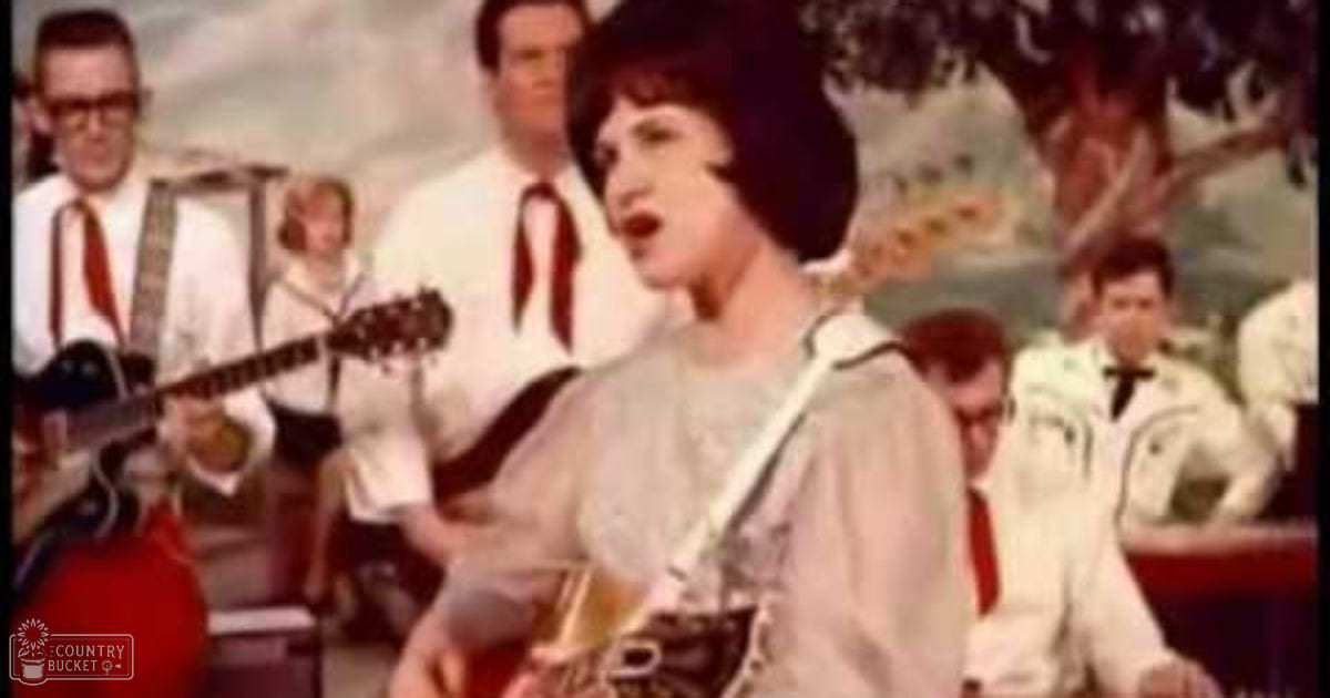 A young adult female singer performing in front of a band with mid-20th century attire on stage, under bright but not harsh lighting.