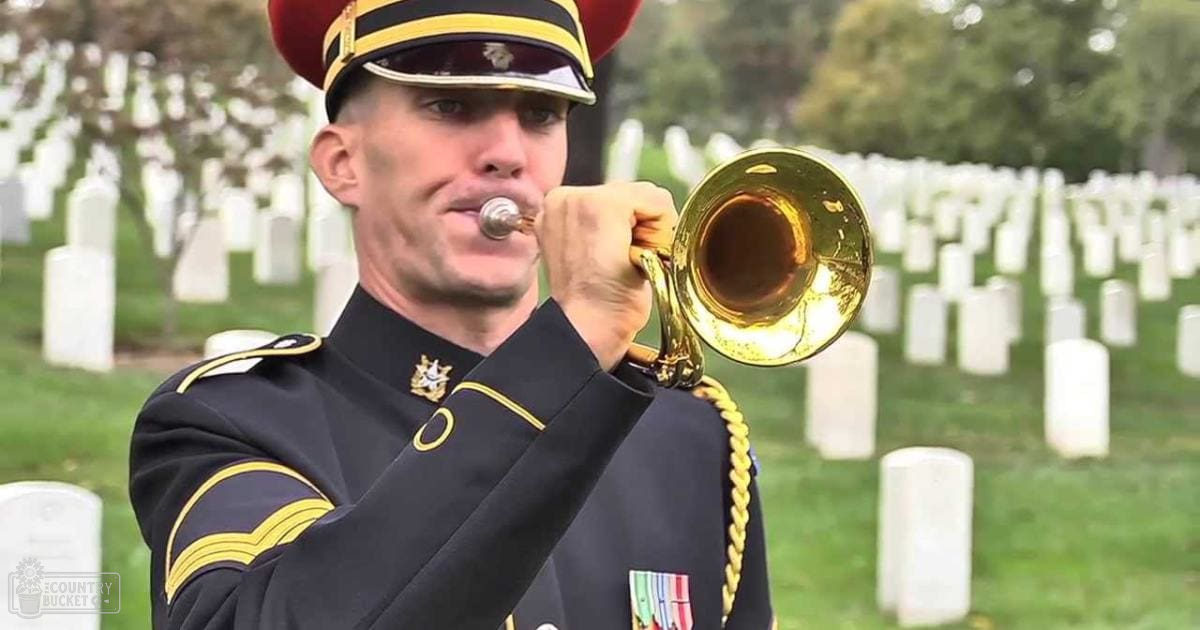 A trumpet player in a dark blue military uniform with gold trim and insignia stands among rows of white headstones at Arlington National Cemetery, late afternoon light illuminating the autumnal scene.