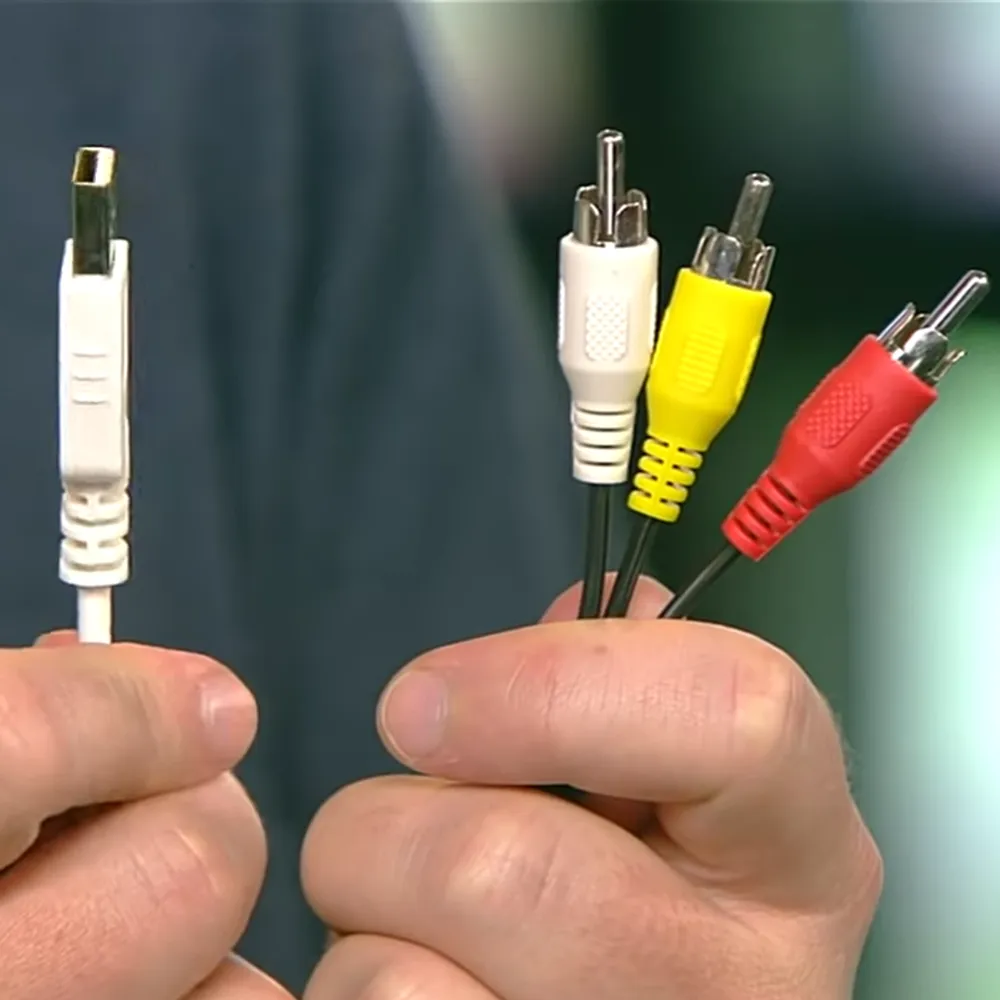 A hand holding audio/video cables indoors with greenish tones in the background