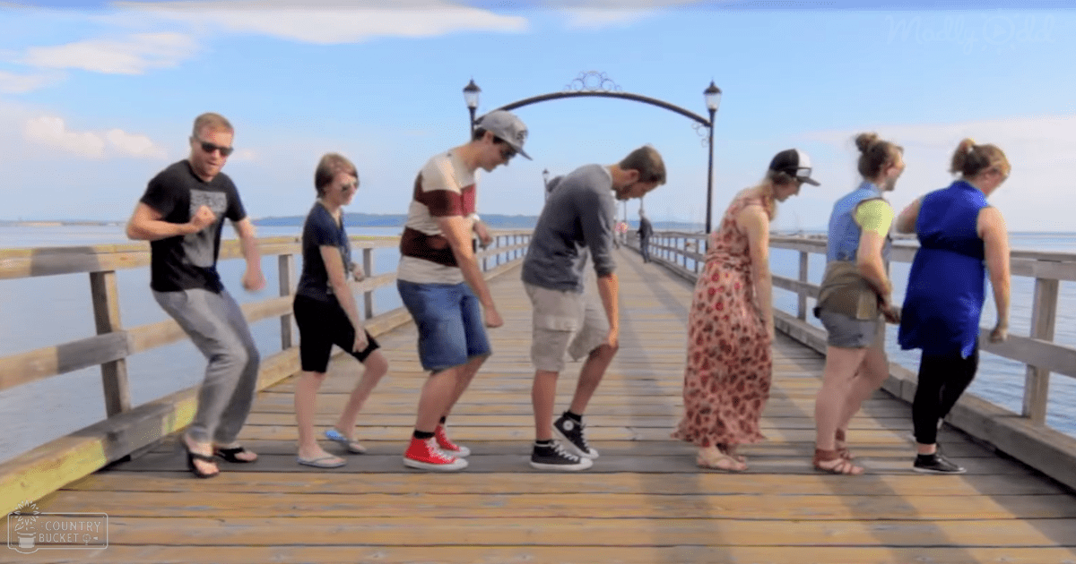 Young adults on a wooden pier near water, wearing casual summer attire; clear sky with street lamps at dusk.