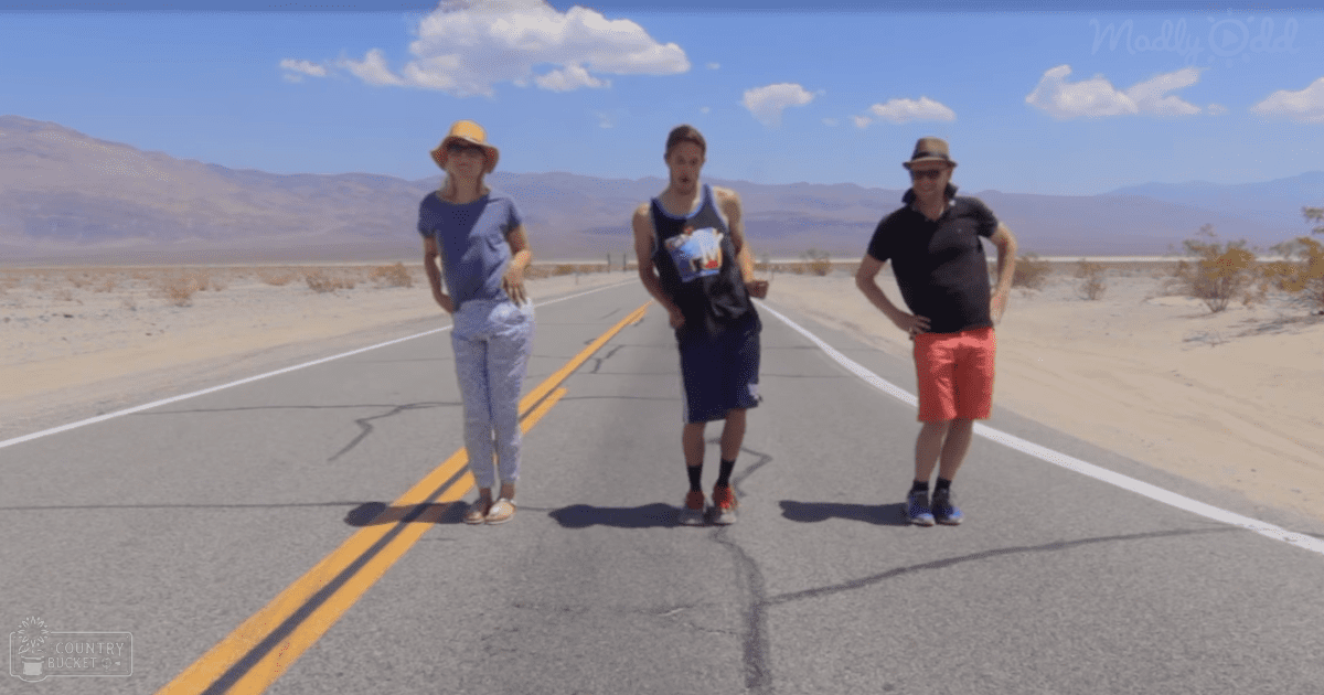 Three individuals standing on an empty road in Death Valley, wearing casual summer attire with a desert landscape backdrop.