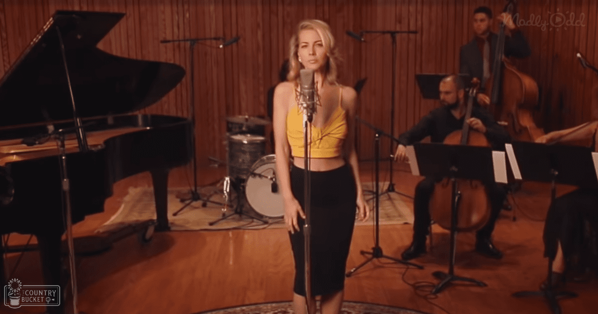 A woman singing in a recording studio with musical instruments and wood-paneled walls.