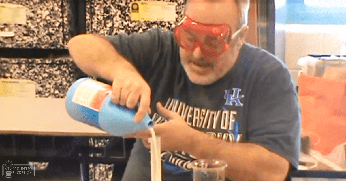 A middle-aged adult male wearing a dark blue T-shirt with 'University of Kentucky' logo, red safety goggles, and standing in an indoor laboratory or workshop setting.