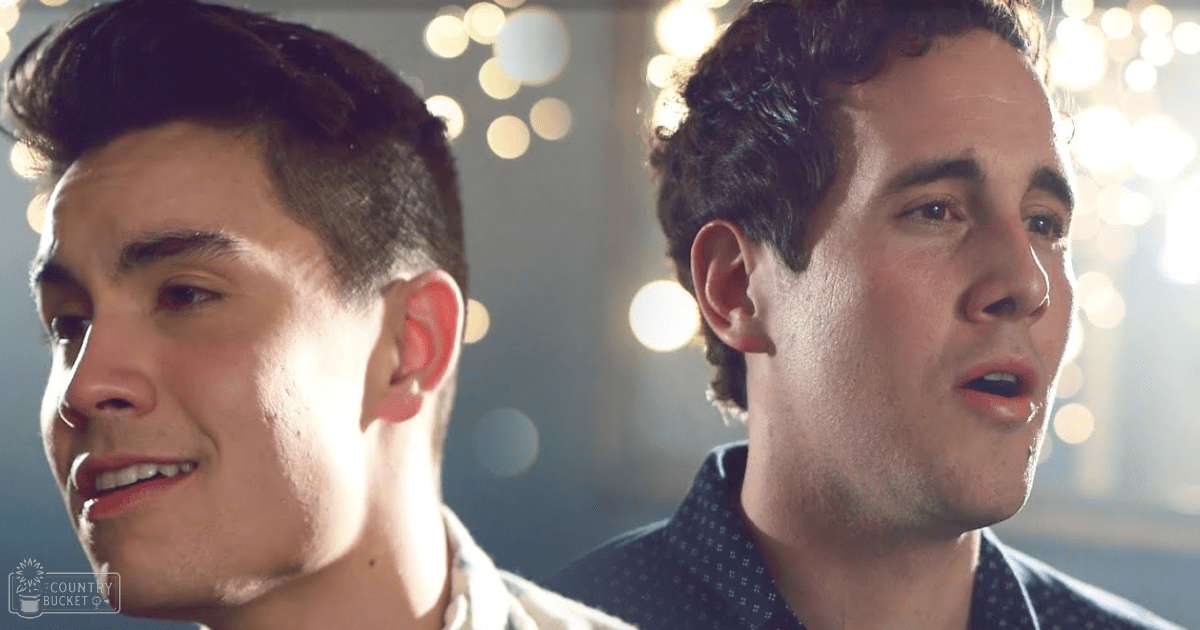 Two young adult males in a dimly lit indoor setting, wearing casual shirts, surrounded by soft bokeh lights.