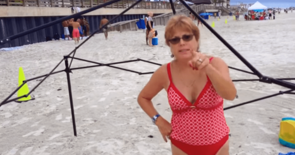 An older adult female wearing a red one-piece swimsuit with white polka dots and a belt, enjoying the beach scene surrounded by other beachgoers.