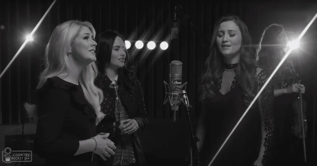 A group of adult female singers in an indoor music studio with stage lighting.