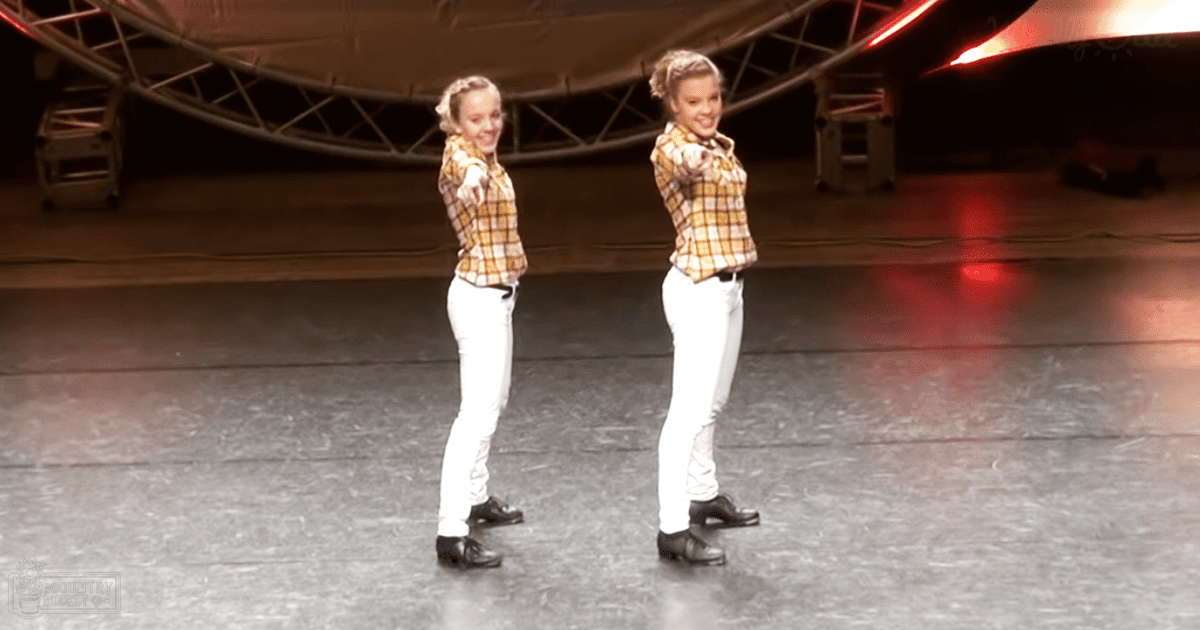 Two young adult females performing a dance routine indoors, wearing white pants and yellow plaid shirts with black shoes.