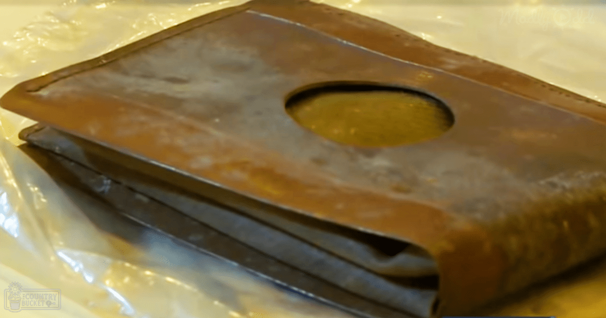 Close-up of worn leather or metal with a circular hole, resting on plastic wrap in an indoor workspace.