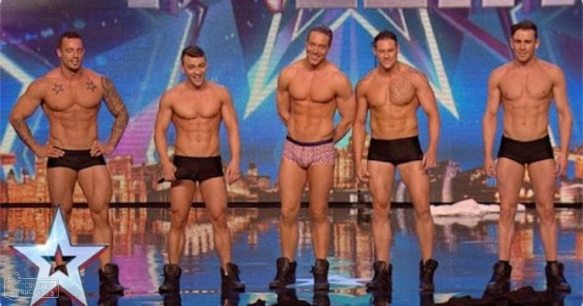 Group of adult male performers in briefs and boots on a talent show stage with cityscape background.