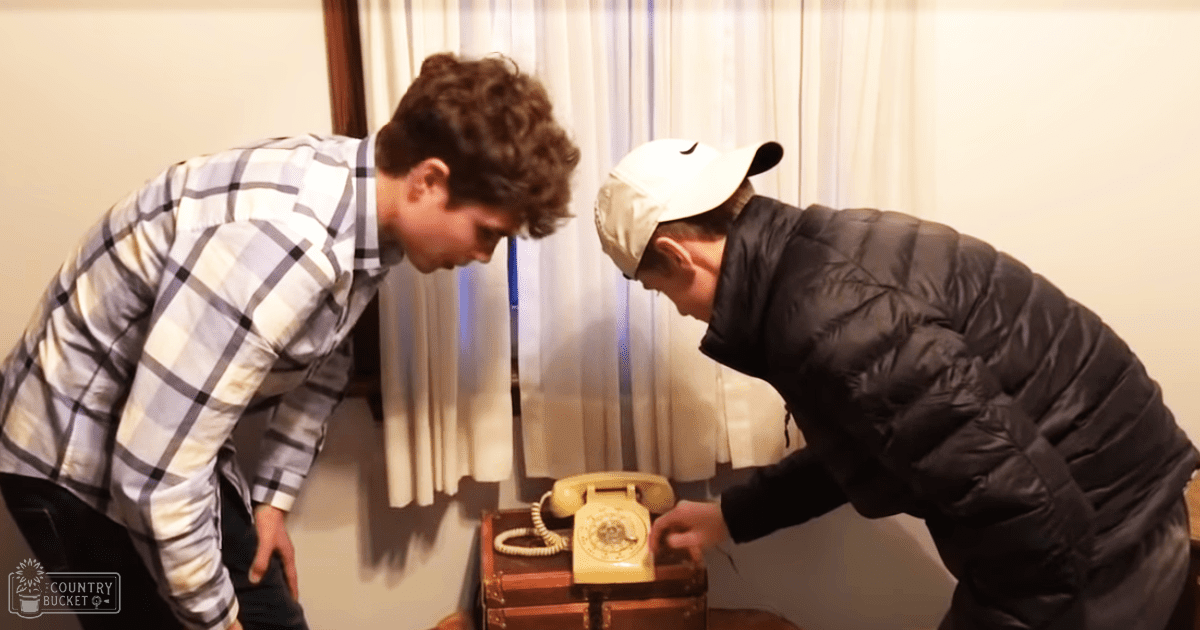 Two young adults interacting with a vintage telephone indoors.