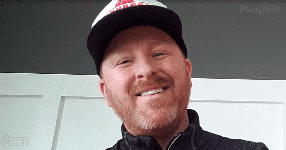 An adult male wearing a dark-colored jacket and a white baseball cap indoors in a casual setting.