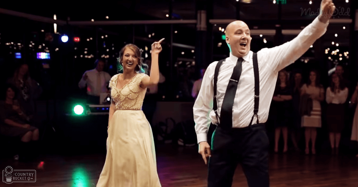 A couple dancing at an indoor event with a green light source and blurred figures of people, suggesting a wedding reception.