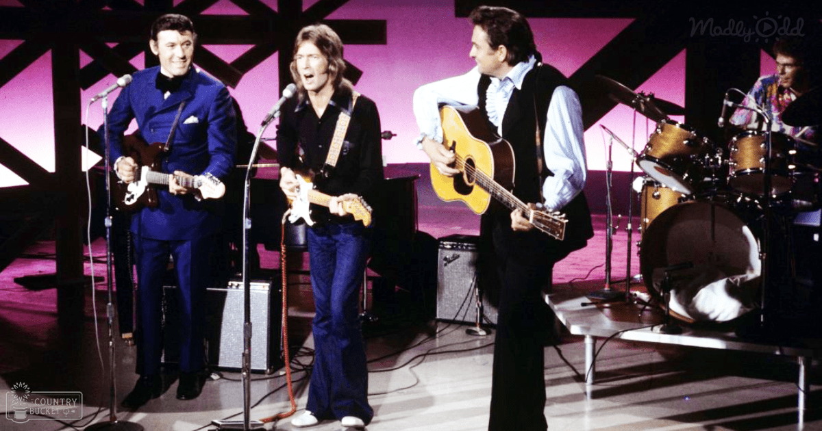 Musical performance on stage with performers, microphones, amplifiers, and a drum set under artificial evening lighting.