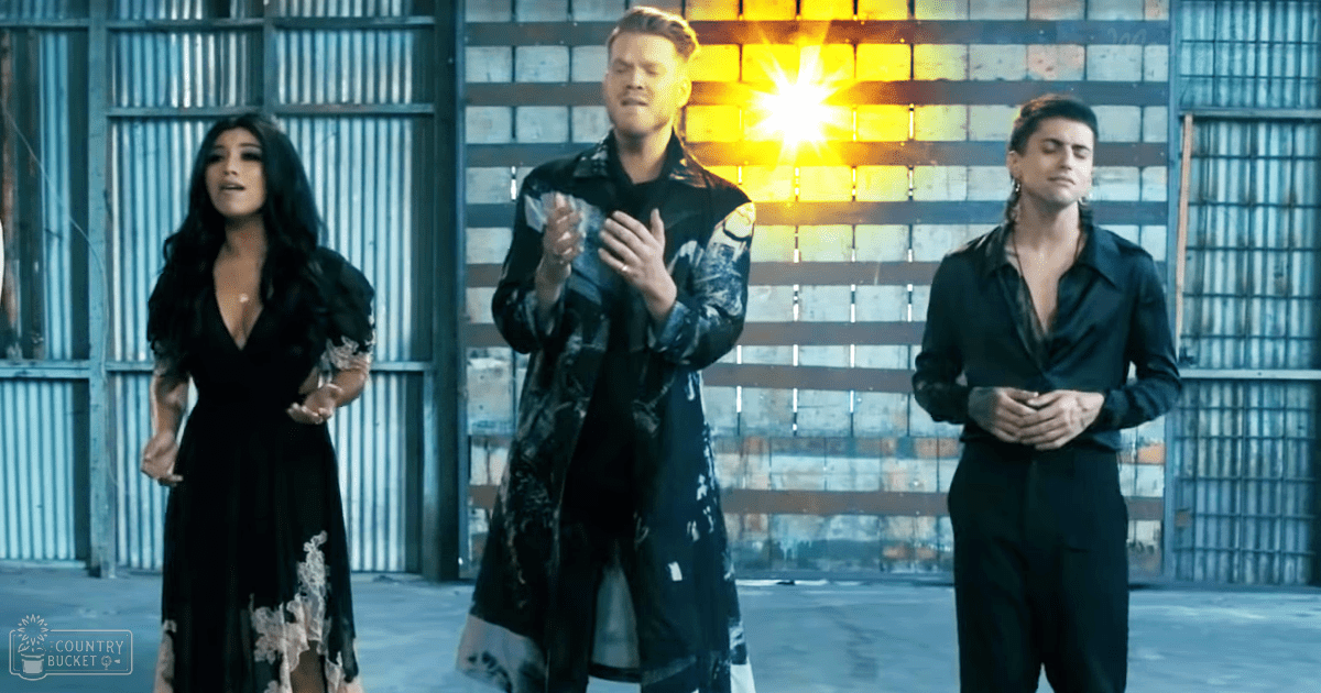 Three young adults dressed casually, standing against an industrial backdrop with natural light streaming through a window during daytime.