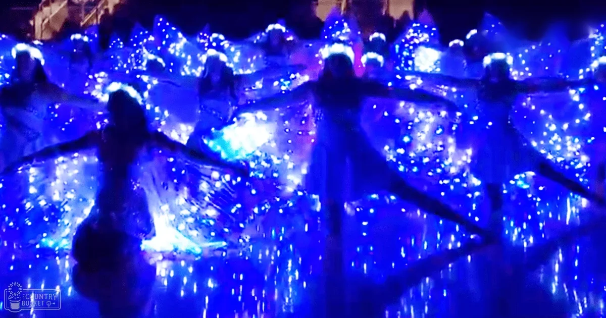 Young adult female performers in an indoor evening event, wearing flowing blue glittery garments with glowing elements scattered throughout.