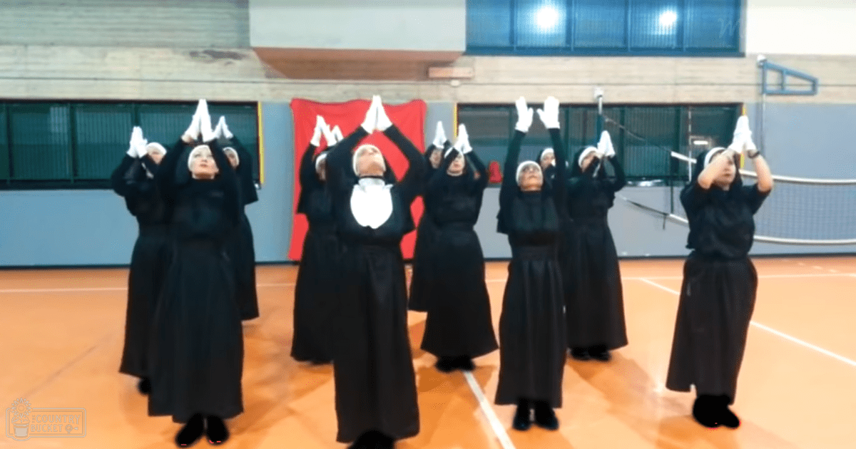 Middle-aged female individuals wearing traditional religious attire, performing indoors within an artificial-lit gymnasium setting.