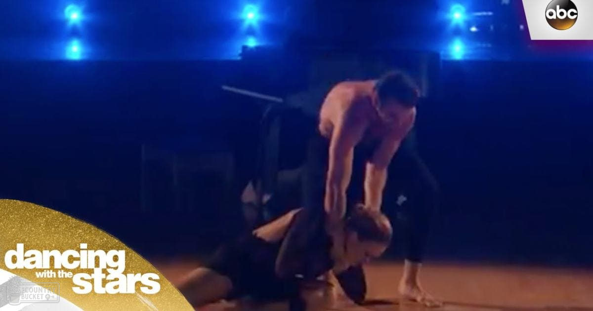 Adult male in black pants and shoes dancing in a dimly lit dance studio with blue stage lights.