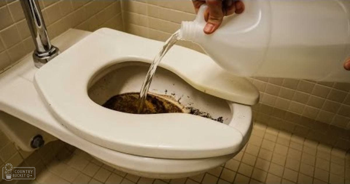 A bathroom scene with a white toilet being cleaned using a plastic jug of water, beige tiled walls, and chrome faucet in the background.
