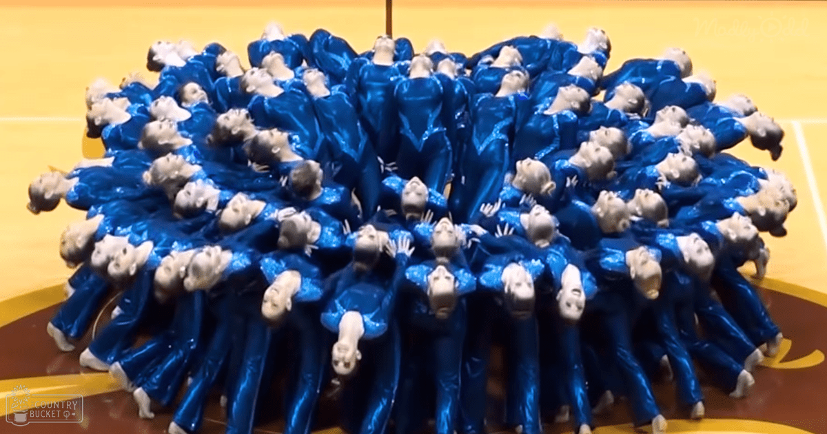 Young adult female dancers performing in a gymnasium with blue reflective dance leotards, artificial lighting indicating an evening setting.