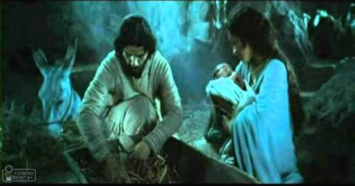A nativity scene set in a stable, with an adult male wearing a hooded woolen garment and an adult female holding a baby wrapped in cloth; a donkey is present on the left. The setting suggests a serene historical atmosphere with muted blues, greens, and browns dominating the palette.