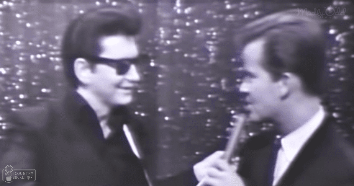 Two adult males perform a musical act indoors under bright stage lights with a backdrop of sparkling effects.