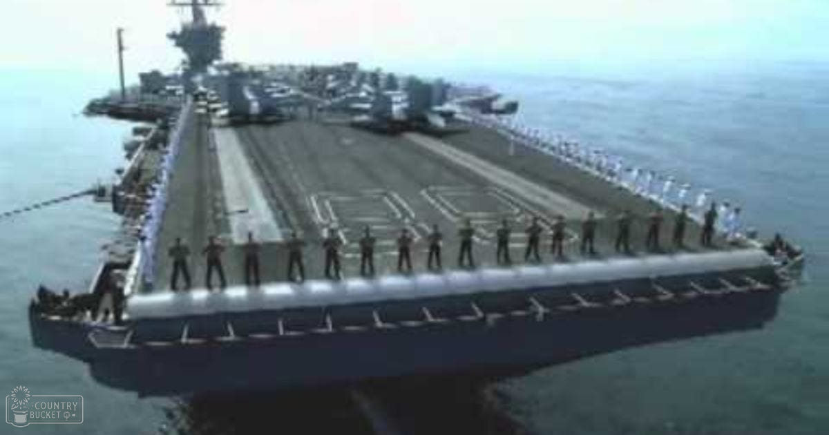 A large aircraft carrier docked at a pier, with an overcast ocean setting under daytime lighting.