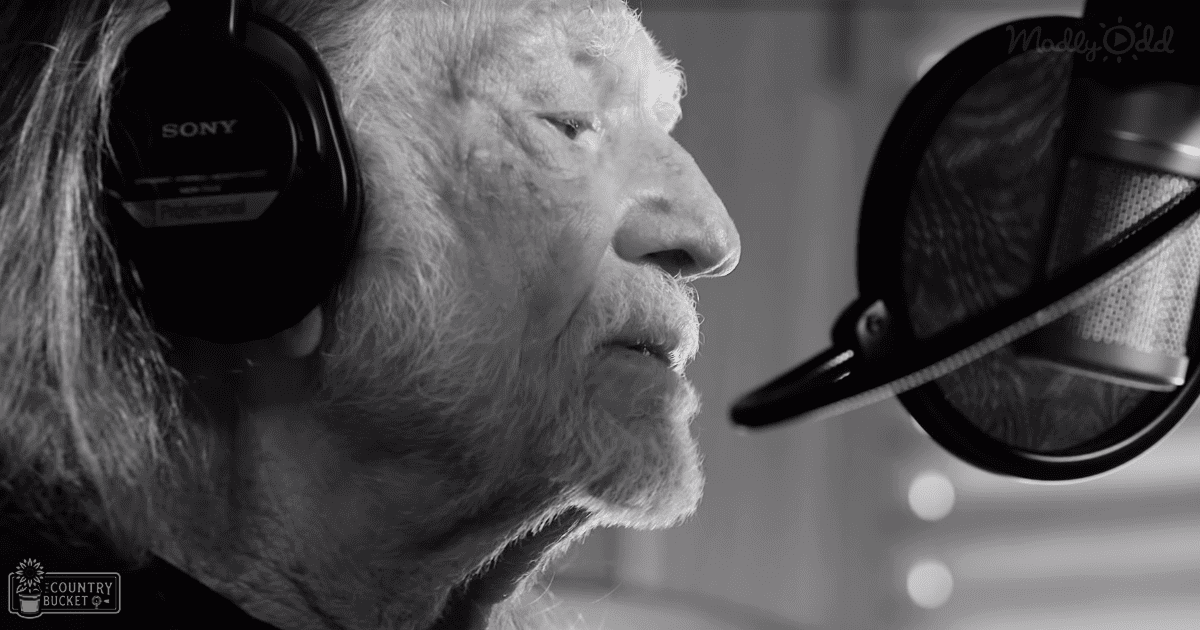 An older adult male in a recording studio wearing a dark shirt or jacket with long sleeves, collared neckline, and Sony headphones.
