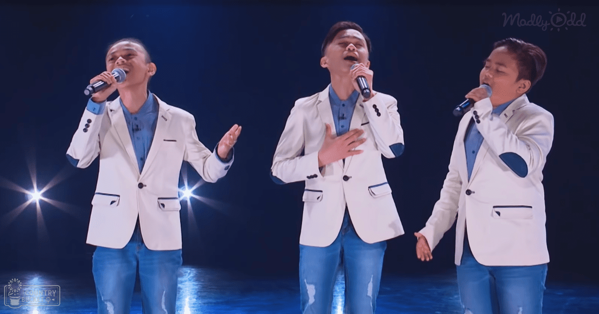 Group performance scene indoors, young adult males in tailored white blazers and blue jeans under dimly lit stage lights creating a dramatic effect.