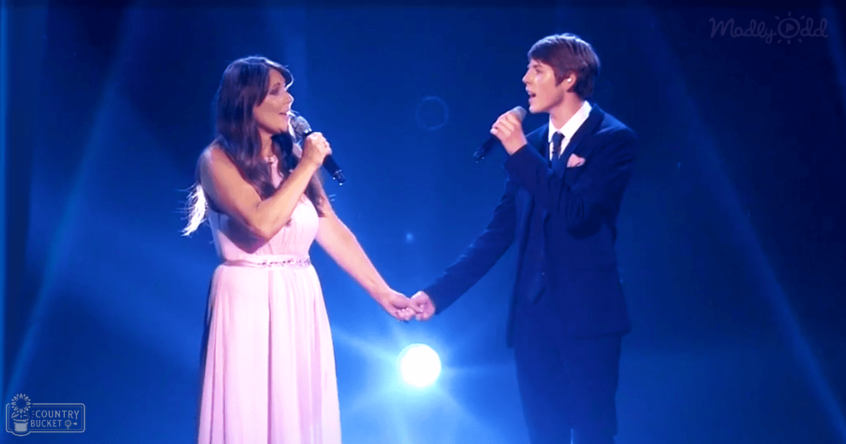 A duet performance scene with two performers, one wearing a light pink dress and the other in a dark blue suit, holding microphones under dramatic stage lighting.