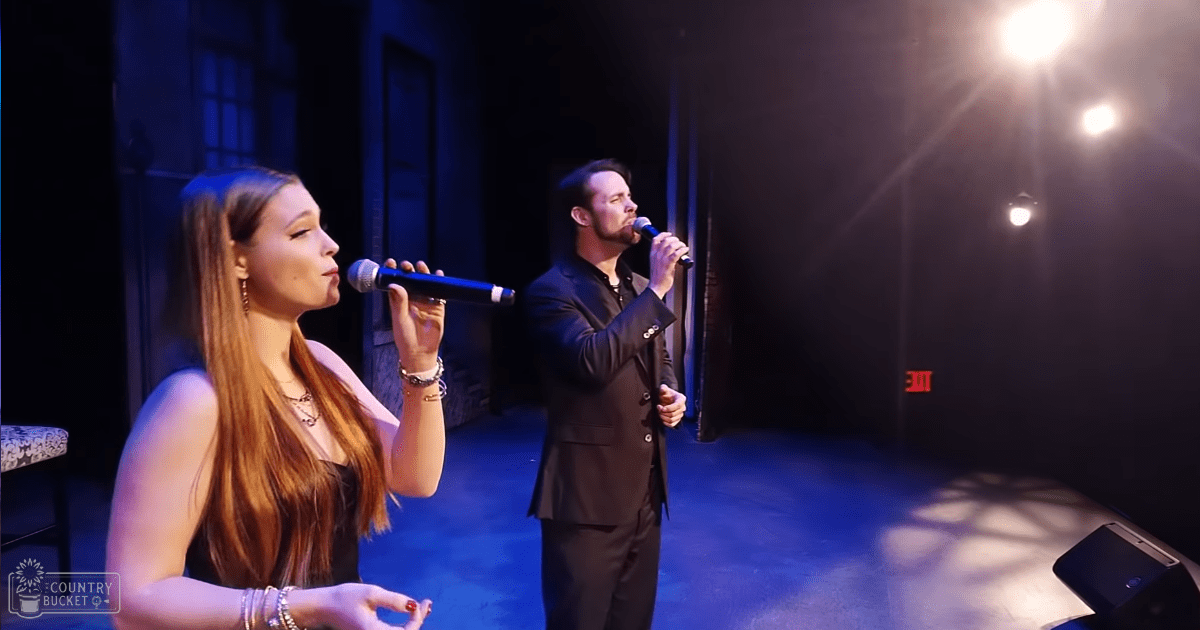 A musical performance at an indoor venue with stage lighting and microphones visible in a dark setting.
