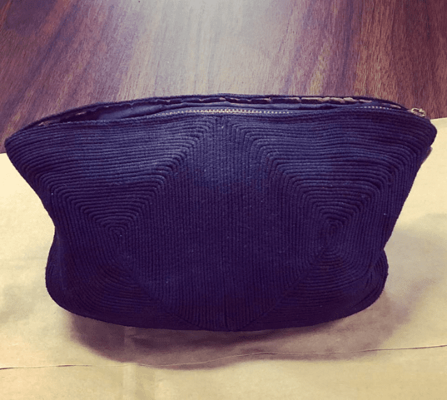 A dark blue corduroy pouch with a zipper, placed indoors on a light-colored surface.