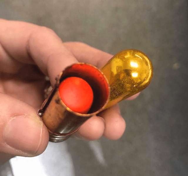 A person holding a small metallic object with red spherical component indoors, likely a workshop or garage setting