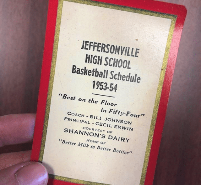 1953-54 Jeffersonville High School Basketball Schedule, framed with red border and gold accents, displayed indoors against a wooden surface.