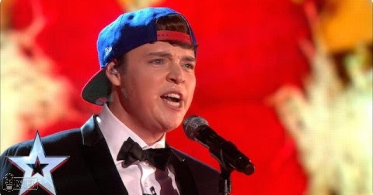 A young adult male in a black tuxedo with star design, singing into a microphone on stage under bright red and yellow lighting.