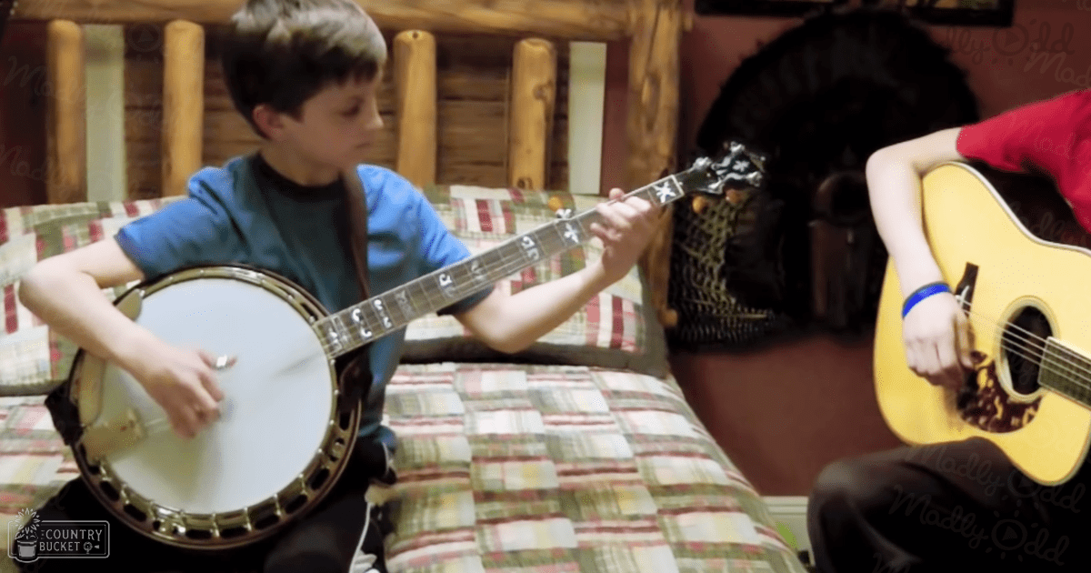 Child playing banjo in cozy indoor cabin setting with natural light, plaid furniture and rustic wooden backdrop