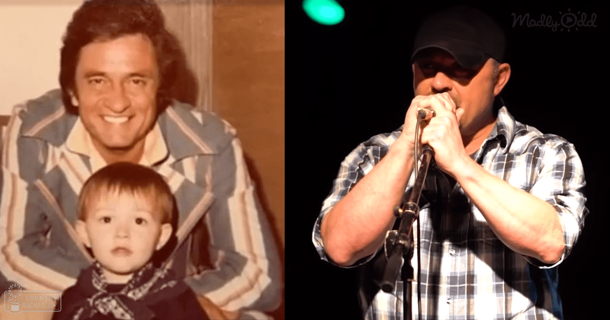 An adult male singer wearing a black cap and plaid shirt performs on stage, holding a microphone; a toddler with light brown hair stands nearby indoors.