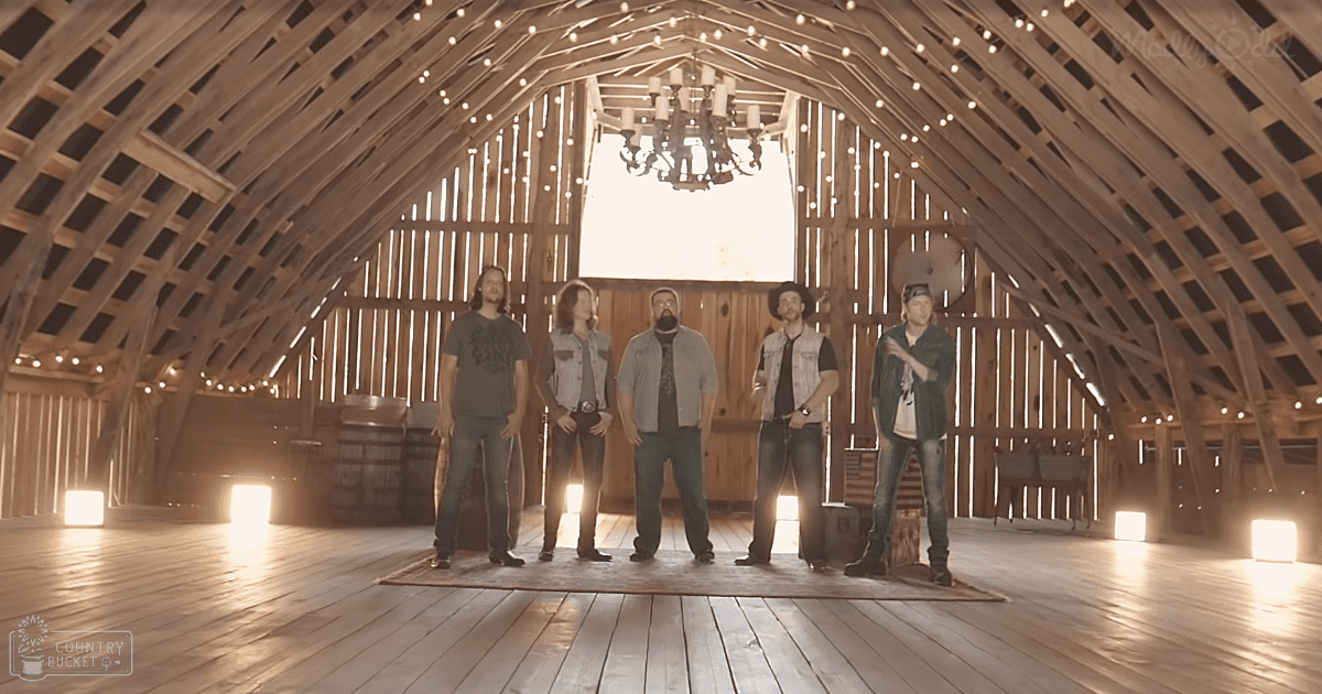 Five adults inside a rustic indoor barn with wooden beams and chandelier, wearing casual attire in warm, late afternoon light.
