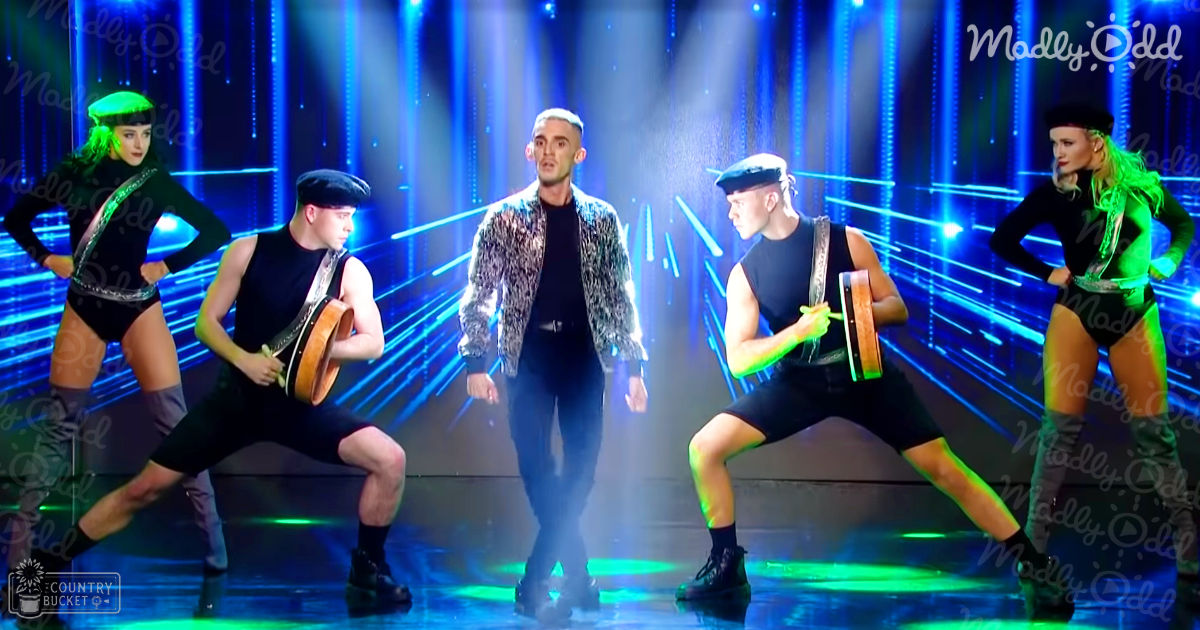 A performance scene with an adult male singer in a patterned jacket, young adults wearing berets and form-fitting black bodysuits, on stage under blue lighting effects at night.