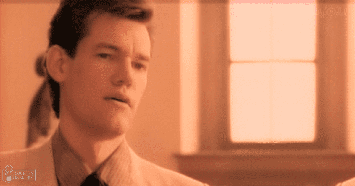 A young adult male in a collared shirt with a dark tie stands indoors, bathed in natural light from an unseen window.