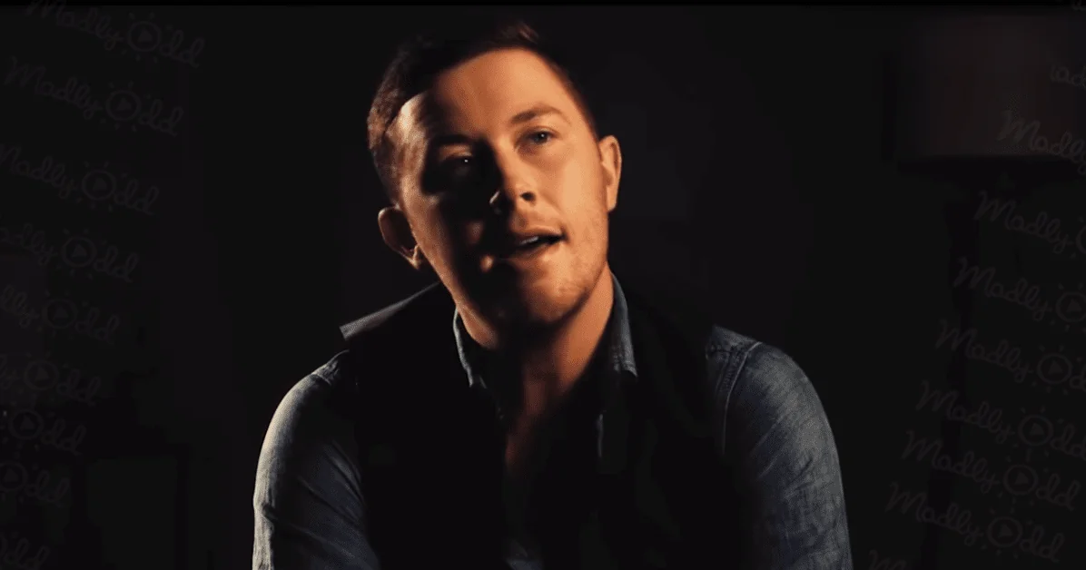 A young adult male in a relaxed fit denim shirt with solid dark blue color and collar, standing against a dark background with 'Madly Odd' text overlay.