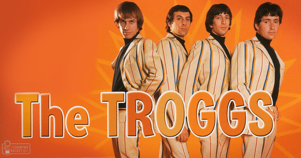 Promotional studio shot for The Troggs music group with four adult males wearing striped blazers over black turtlenecks against an orange starburst background, likely from the 1960s or early 1970s.