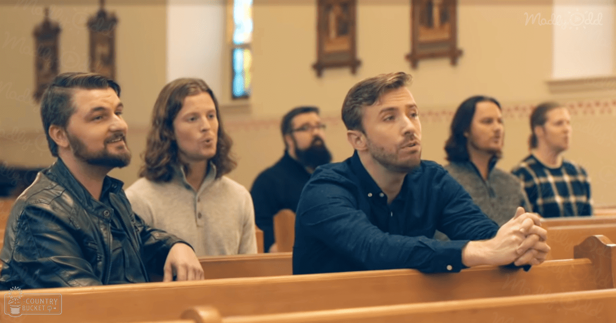 A group of young adult males in a church setting with wooden pews, stained glass windows, and religious iconography.