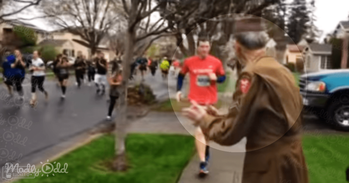 Adult male marathon runner wearing red t-shirt with race bib, running on a residential street during an overcast day in what appears to be spring or fall.