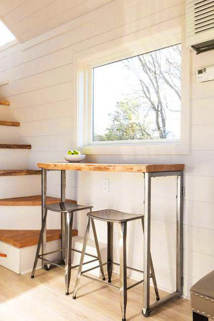 A small indoor setting with wooden table, metal stools, white walls, and a window showing bare trees outside.