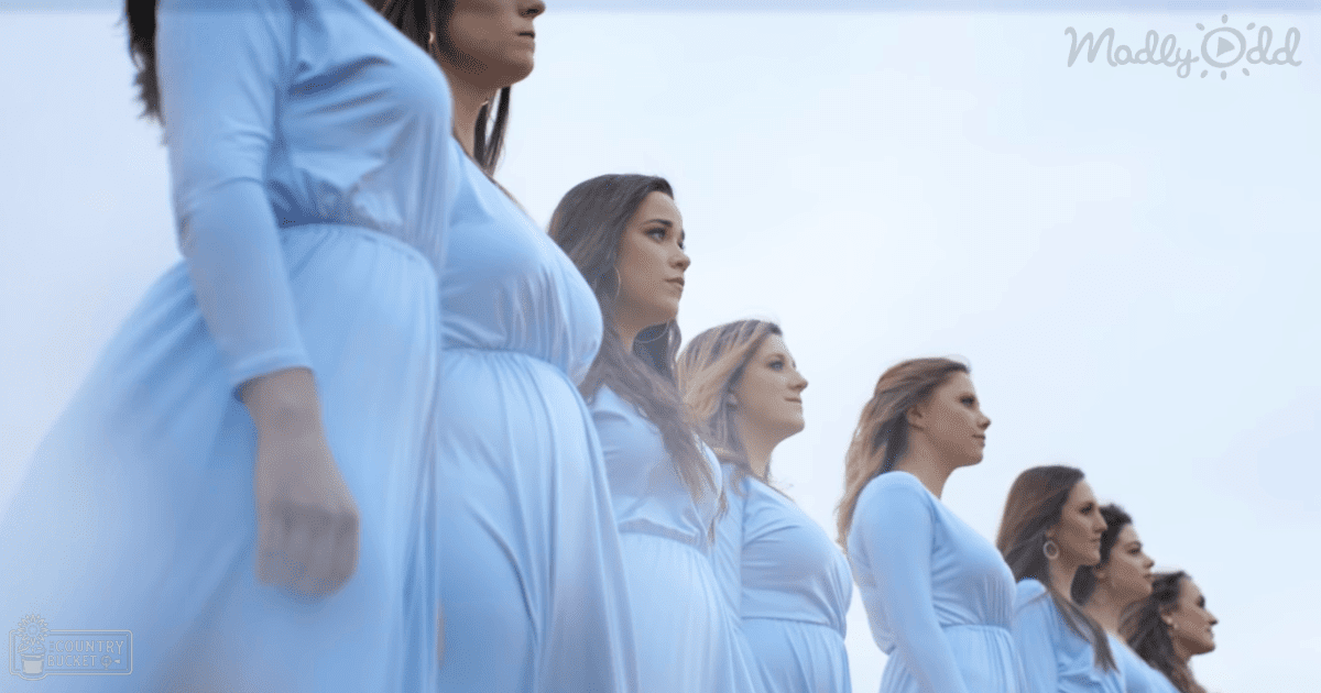A group of adult female pregnant women in light blue dresses, standing outdoors under a clear sky during late afternoon or early evening.