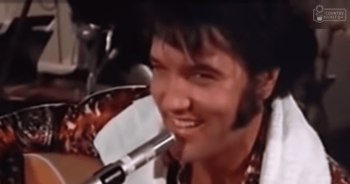 A young adult male wearing a white shirt with a patterned design and a dark tie, standing on what appears to be a stage with musical instruments and artificial lighting in the background.