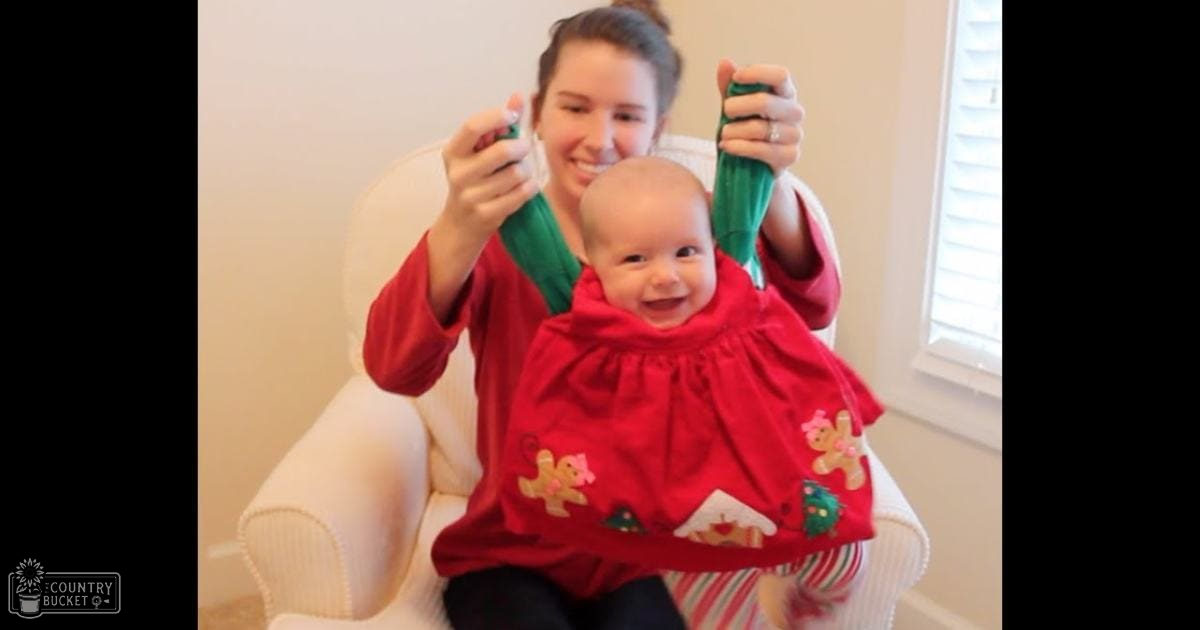 An infant in a red dress with gingerbread man patterns being held by an adult wearing a red long-sleeved top and green trim, set against a white indoor background.