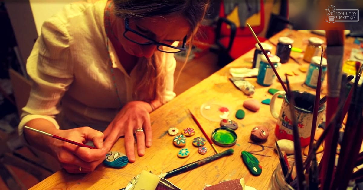 An adult female artist at an art studio, working amidst crafting materials under warm indoor lighting.