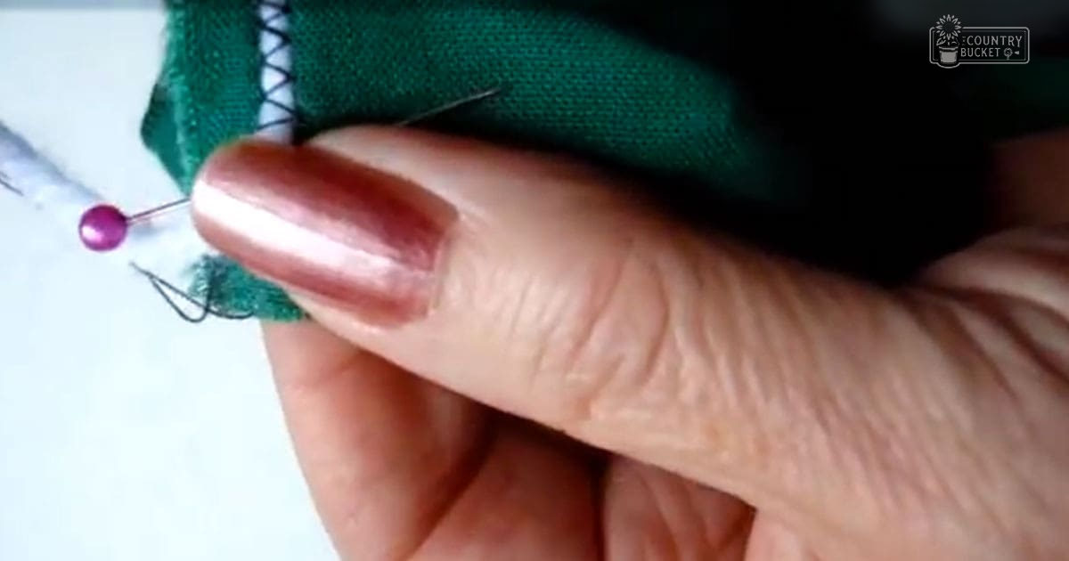 Close-up of hands working with dark-colored fabric and green section on a plain white background, possibly sewing activity