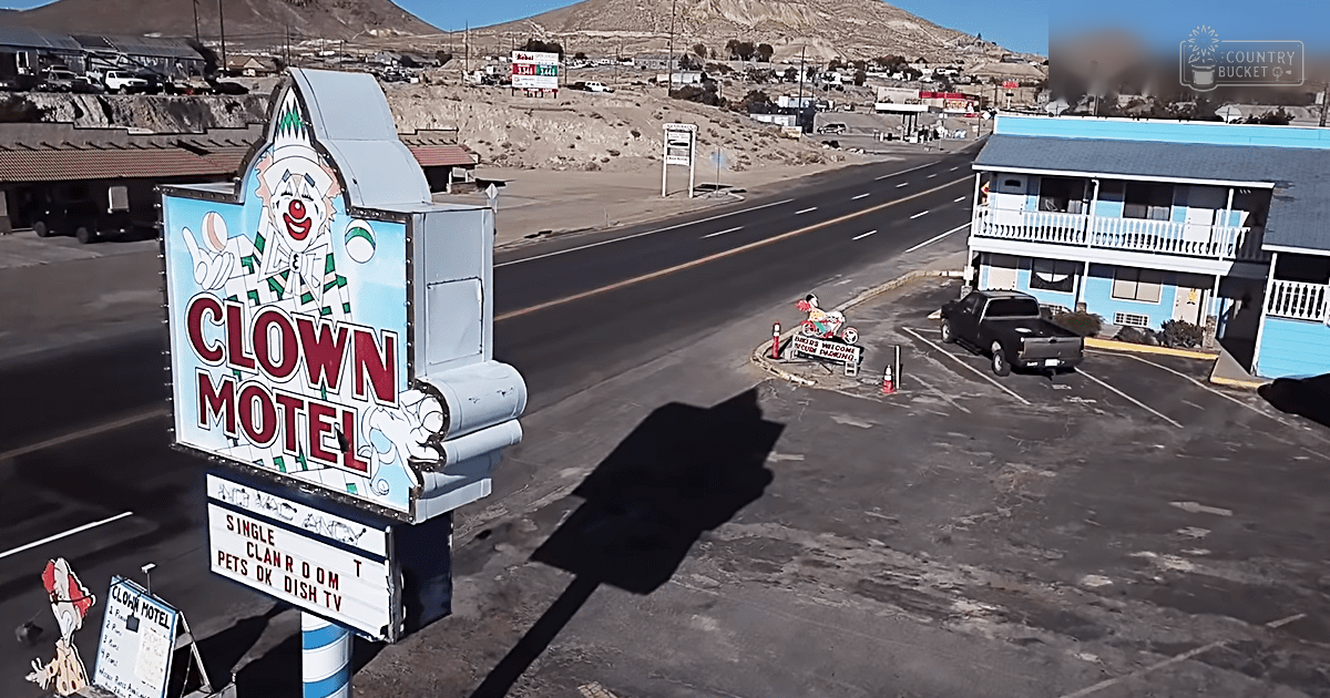 Clown-themed motel sign in a desert town with clear skies, midday light, blue building, black pickup truck.